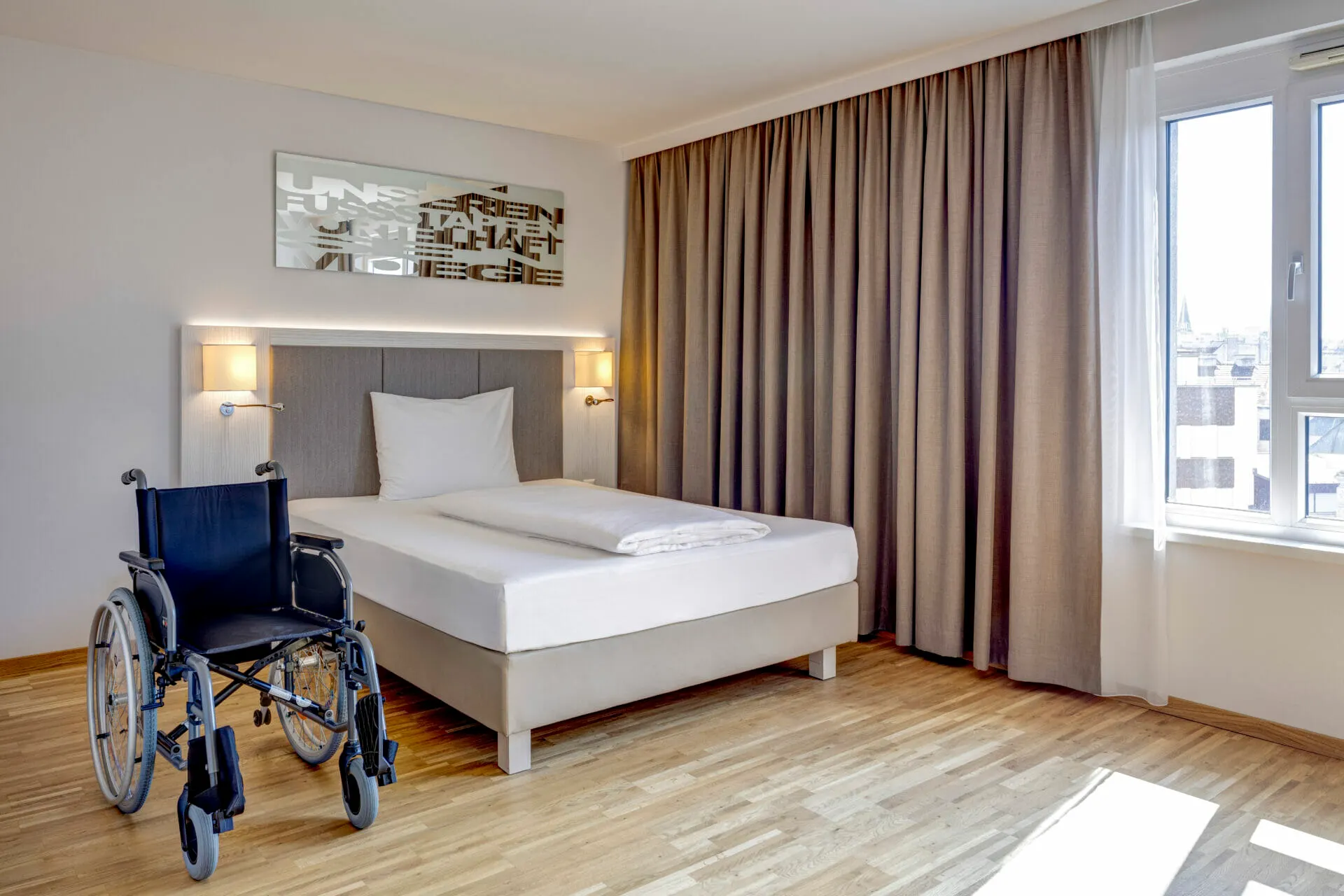 Zimmer Barrierefrei: Bett mit viel Bewegungsfläche, daneben ein Rollstuhl