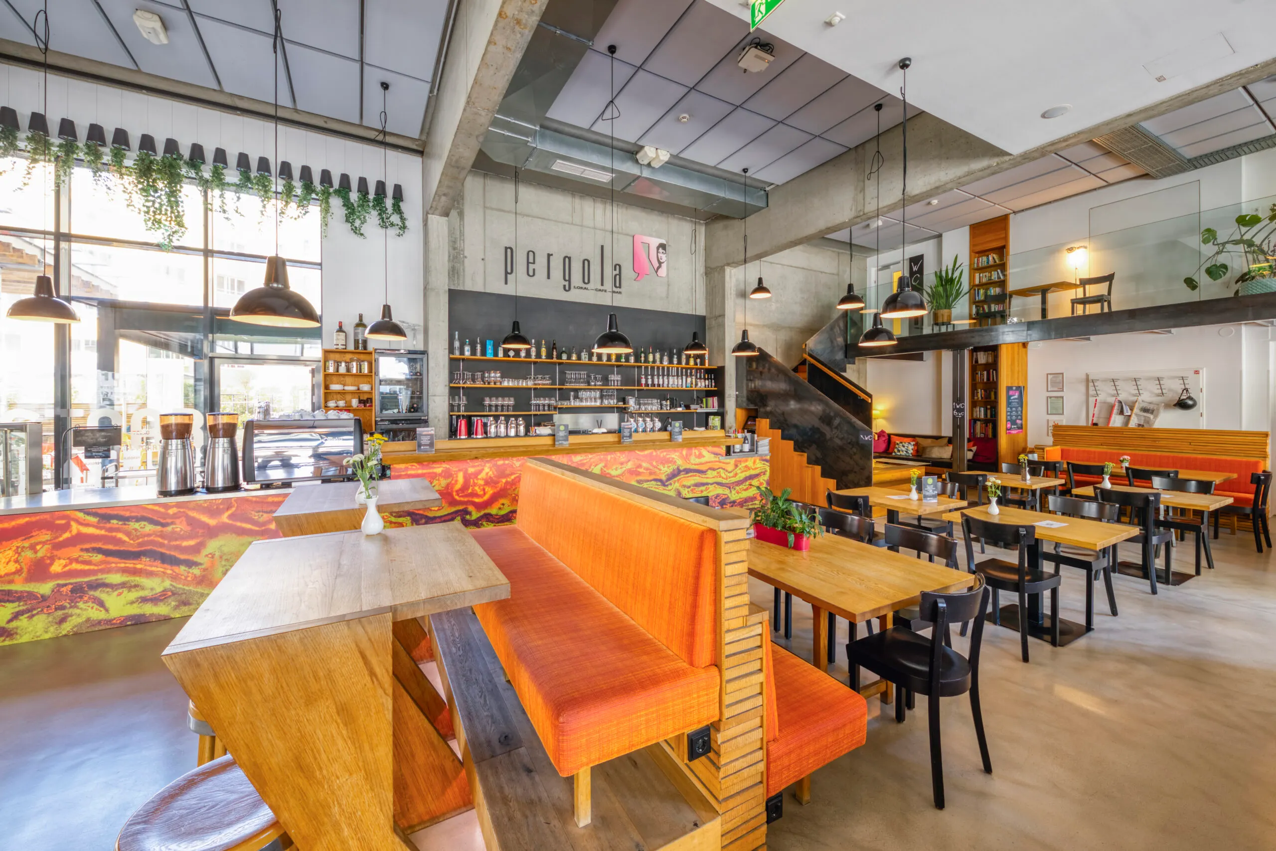 Die Pergola: orange Bänke, Holztische, Galerie und Bar